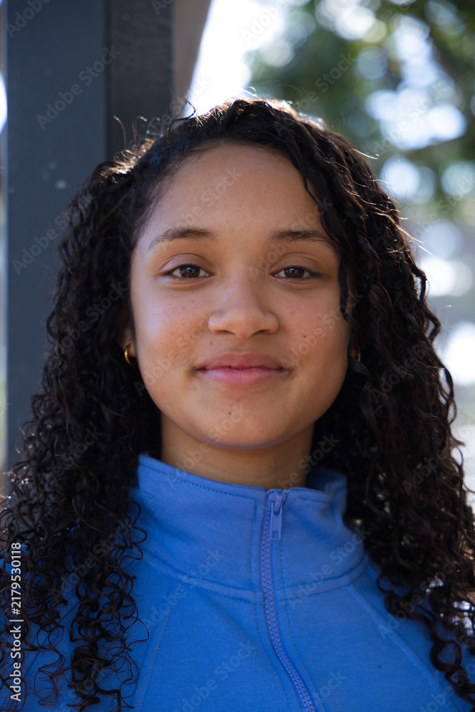 Obraz premium African American teenage female smiling wearing blue fleece, gold hoop earrings at park near pillar