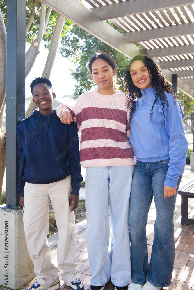 Obraz premium African American youths posing under slatted pergola at campus plaza, wearing hoodies and jeans