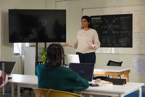 Diverse participants listening while Indian presenter gesturing by whiteboard and screen in class