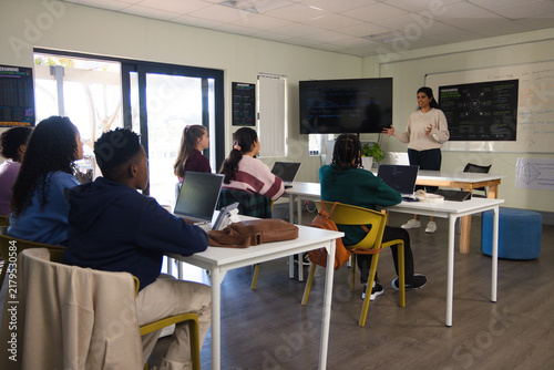 Indian teacher teaching youth students in classroom with laptops whiteboard wall monitor