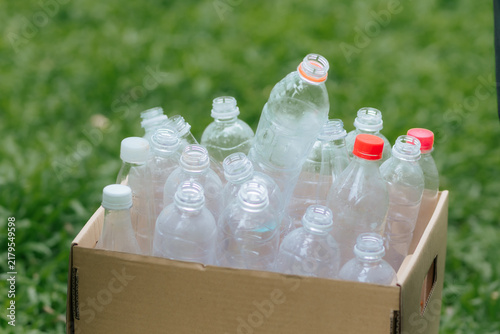 Картината върху платно Happy young woman holding a cardboard box full of plastic waste, smiling at the camera to promote environmental conservation and recycling