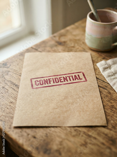 Brown envelope with a red confidential stamp beside an ombre glazed mug