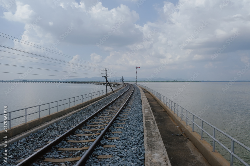 Fototapeta premium Railway track bridge over water, infrastructure beneath cloudy sky