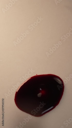Blood dripping into dense red pool on plain surface for trauma scene analysis, top view macro slow motion, top copy space, vertical video