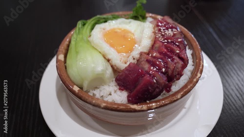 Close-up of a traditional Chinese BBQ pork rice bowl served in a ceramic bowl, featuring sliced char siu pork, a sunny-side-up fried egg, steamed bok choy, and white rice, topped with sesame seeds.