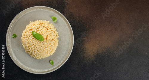 Obraz na płótnie Plate of cooked couscous garnished with fresh basil leaves on a textured dark background, showcasing the fine grains and culinary presentation