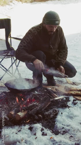 Man cooking food over campfire in snowy forest