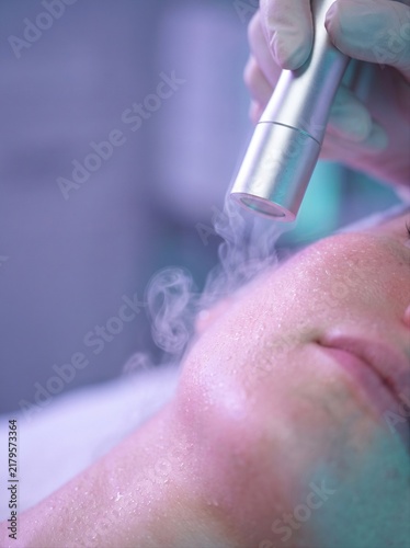 Therapist holds the cryotherapy nozzle to woman's cheek, with light frosty steam visible in the frame. Cryotherapy treatment, aesthetic cosmetology concept. Close-up shot for commercial poster