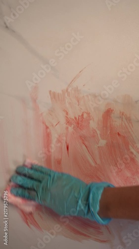 Blue gloved hand wiping blood streak for crime scene forensic sanitation and evidence concealment, top view slow zoom in, top copy space, vertical video