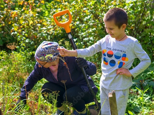 Foto Boy holding tiny carrot harvest while gardening with mother in sunny backyard, h