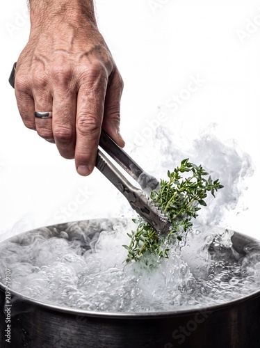 Chef hand using metal tongs to blanch fresh green herbs in boiling water, stainless steel pot with steam on white background