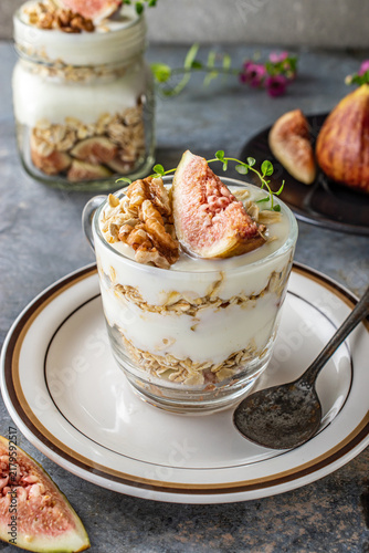 Healthy Greek yogurt parfait layered with wholesome rolled oats, fresh figs, walnuts, and natural honey served in glass jars. Delicious organic clean eating breakfast for wellness lifestyle.
