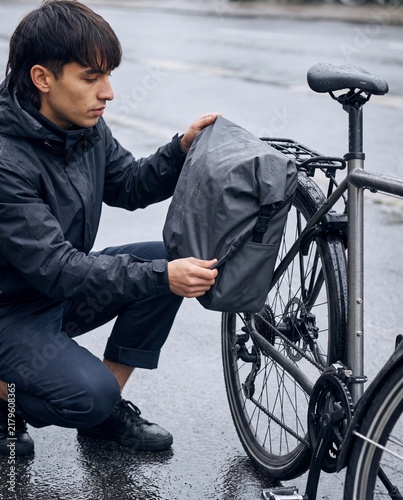 Cyclist fitting a rain cover over a pannier on wet pavement