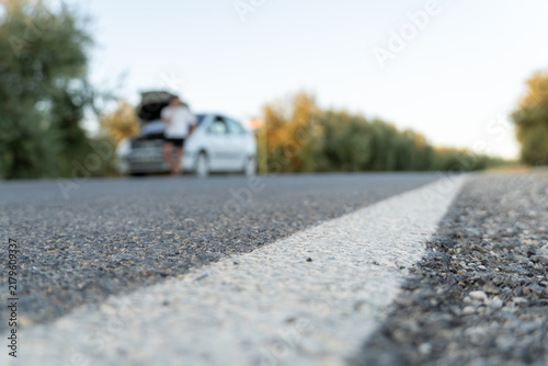 Fotografie Person standing beside a broken down car with open hood on the side of a rural r