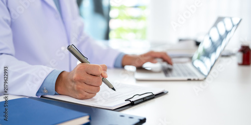 Doctor looking at laptop screen writing in notebook for research planning or medical tech innovation in hospital office. Healthcare medic worker, research strategy book notes and online communication.