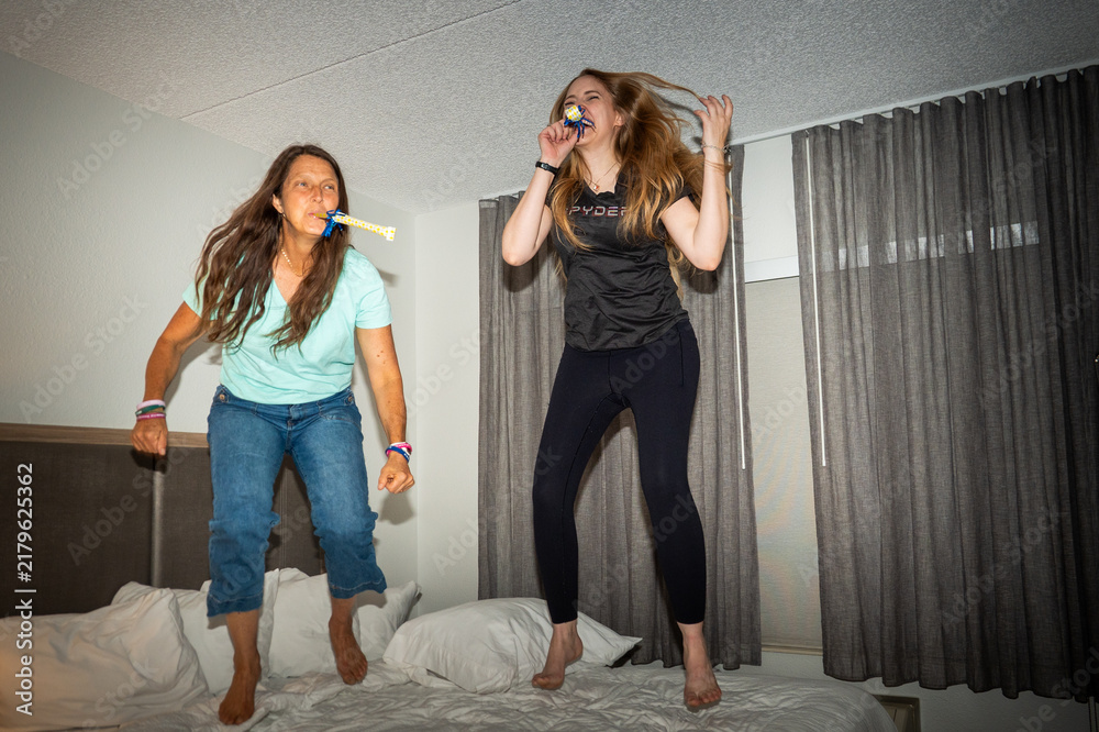 Naklejka premium Women Jumping on Bed During Indoor Celebration With Party Blowers
