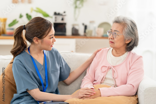 Young Asian female nurse comforts senior Asian woman during health discussion in assisted living center, offering compassionate nursing care, emotional support, communication, reassurance, trust.