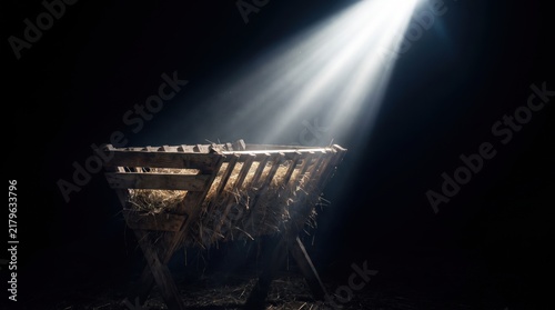wooden manger filled with hay illuminated by bright divine light in dark space. nativity scene concept. christmas religion symbol. banner, website header with copyspace.