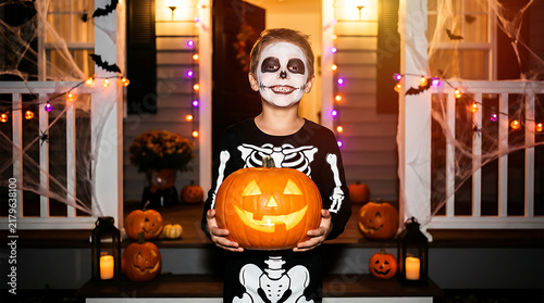 A young child wearing skeleton face paint and a costume holds a glowing jack-o'-lantern in a foggy backyard created with generative AI.