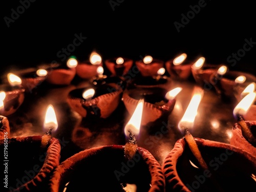Fotografie A close-up shot of multiple traditional earthen oil lamps, known as Diya, beautifully illuminated and arranged on a metallic tray in the dark