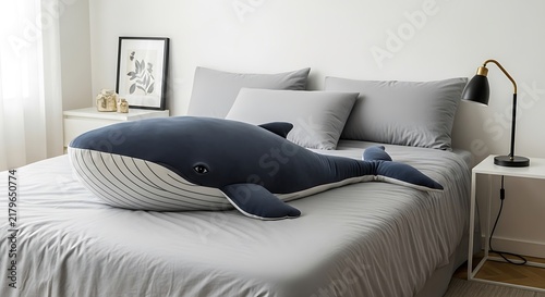 Large blue whale plush toy lying on a comfortable bed with grey sheets in a modern bedroom interior