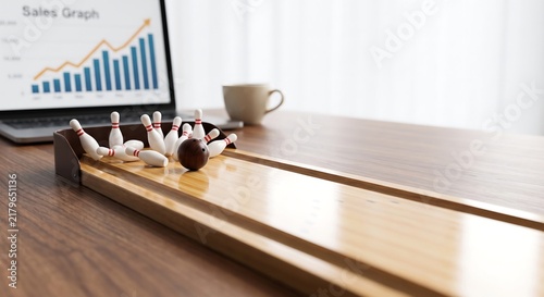 Miniature bowling game on office desk with business sales graph on laptop screen