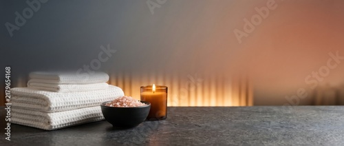 Spa wellness background with white towels, burning candle and bath salts on dark stone