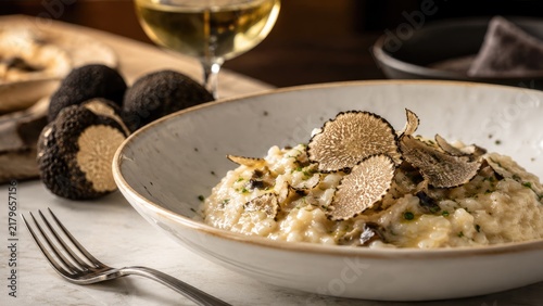 Creamy arborio risotto topped with shaved black truffles, plated elegantly with a wine glass and rustic tabletop