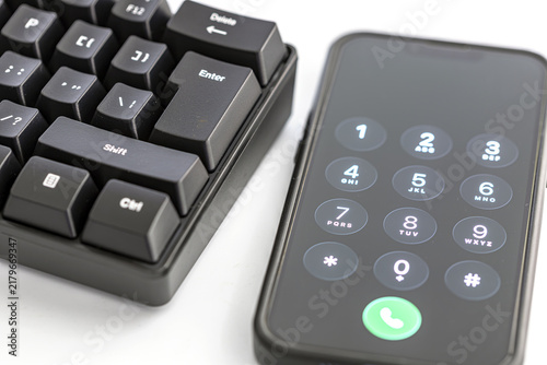 Detailed close-up of a black mechanical keyboard featuring the Enter key, positioned next to a smartphone displaying a dial pad with numbers and a glowing green call button ready to connect