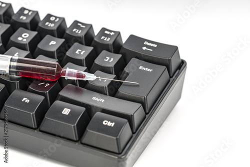 Conceptual image showing a syringe with red liquid resembling blood placed close to the enter key of a black computer keyboard, representing health consequences of digital actions
