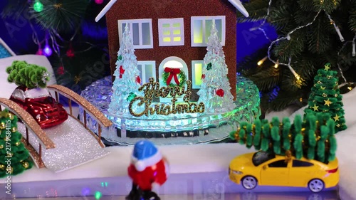 In the center of the Christmas village, among the decorated Christmas trees, Santa Claus comes galloping to a brown house with lights