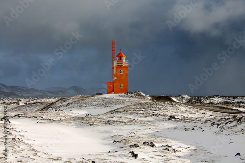 Orange lighthouse on a stony coast in Iceland. Winter landscape