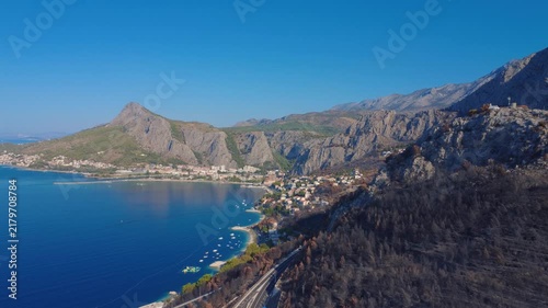 Aerial view of a Croatian coastal bay with mountains, a town, boats, and a burned hillside after a wildfire.