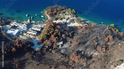 A drone view over fire-damaged woodland, villas, boats, and a small bay along the Croatian coast.