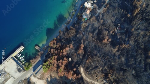 A drone view over the Croatia coastline shows burned forest, clear turquoise water, moored boats, and homes beside a coastal road.