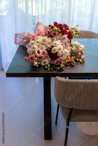 Large bouquet of white and pink flowers on dark wooden dining table in modern interior