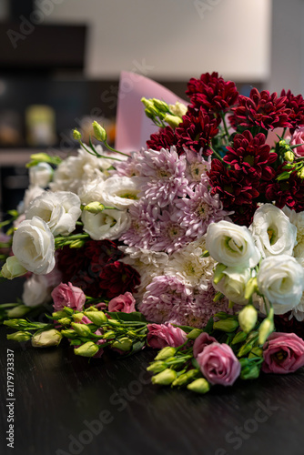 Close-up of rich floral bouquet with white eustoma and burgundy chrysanthemums on dark wooden surface