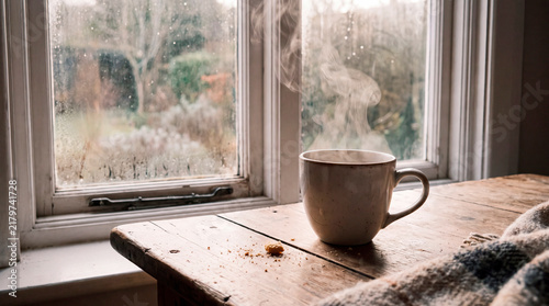 Steaming mug sits on weathered windowsill overlooking rainy garden in cozy autumn calm