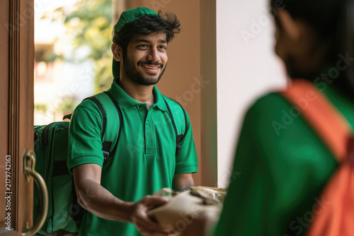 Indian young food delivery boy delivering parcel at doorstep and smiling
