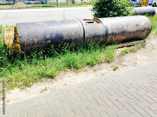 Large Industrial Pipe Sections Lying Beside Roadside Pavement and Overgrown Grass Near Construction Site.