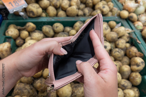 A person showing an empty wallet in a grocery store. A person holding an empty pink wallet against the background of potato crates, lack of funds, financial difficulties