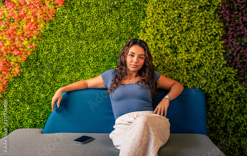 Fotografie Young woman relaxing on sofa against green wall