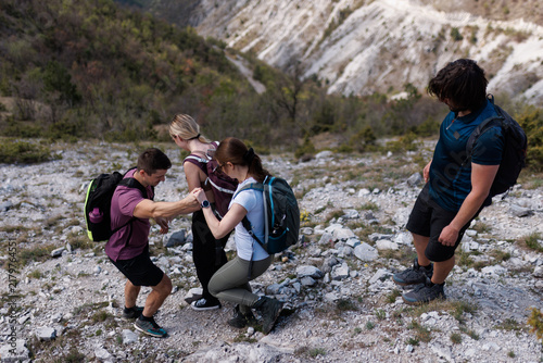 Quadro su tela Four friends hiking together on a rocky mountain trail helping each other during
