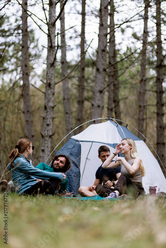 Group of friends enjoying a camping trip in a forest during spring while sitting outside their tent and sharing stories on a sunny day