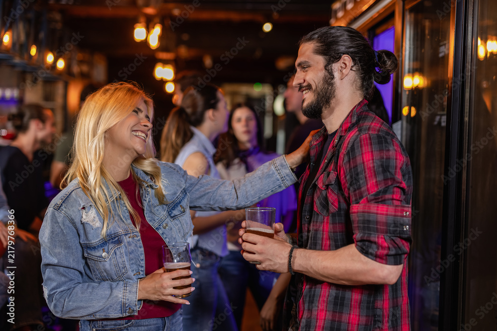 Fototapeta premium Blonde Woman and Young Man Chatting at Lively Pub