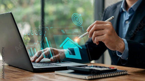 Businessman working with digital real estate graphics, financial charts, and laptop at office desk