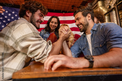 Fotografie Young Men Competing in Arm Wrestling at a Pub