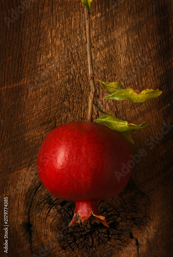 A single Pomegranate hanging in front of a rustic wood board