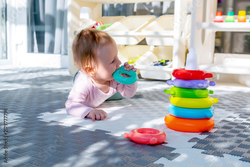 Cute adorable baby child girl playing pyramid toy at home,lying on stomach.toddler building tower of rings.Children logic development,early sensory education,happy childhood