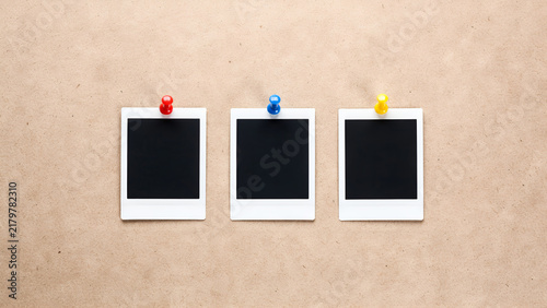 Three blank instant photo frames pinned on a textured brown cork board background, copy space for your photos or text
